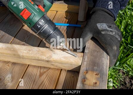 Close up of DIY joiner man person fixing mending wooden wood fence fencing panel with cordless power drill tool England UK Britain Stock Photo