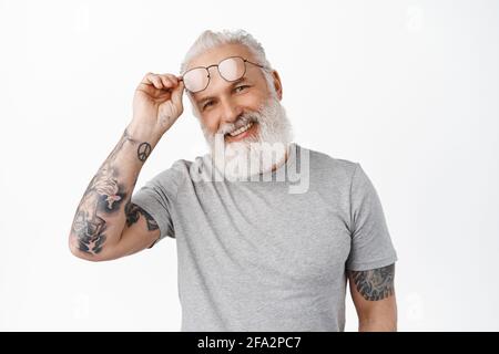 Close up of happy handsome mature man takes-off glasses and smiles at camera, laughs candid and sincere, standing in grey t-shirt against white Stock Photo