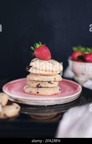 Chocolate chip cookies with strawberry in a pink plate on a black wooden background, close up, still life photography Stock Photo