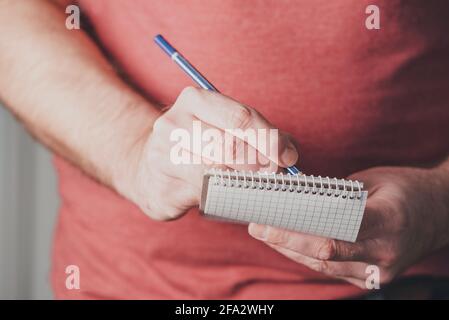 close-up of man taking notes on small spiral notepad using a pencil Stock Photo