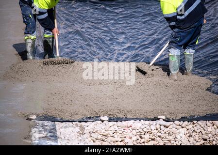Two construction workers at work pouring a mixture on a floor with a plastic sheet. Stock Photo