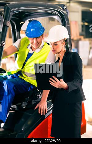 Forklift driver and female super visor with clipboard at warehouse of freight forwarding company Stock Photo