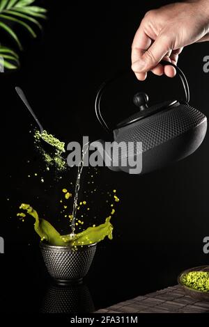 Water poured into a dark cup of matcha tea on a black background. Vertical format. Stock Photo