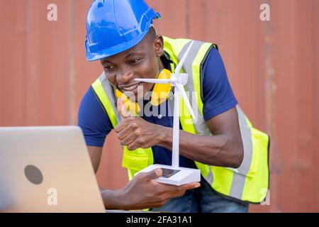 Engineer African American black worker discussing of solar energy from wind turbine model and online with laptop at construction site. Stock Photo