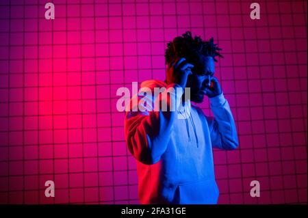 the concept of music. A black man listens to music with headphones on against a background of neon light. Red and blue background Stock Photo