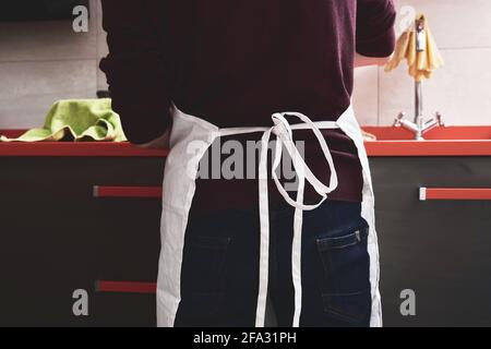 Unrecognizable young caucasian man in apron washing or doing the dishes in a kitchen. Housework concept. Stock Photo