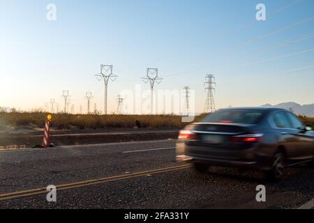 Electric pylons at sunset. Cars drive by on street.  Stock Photo