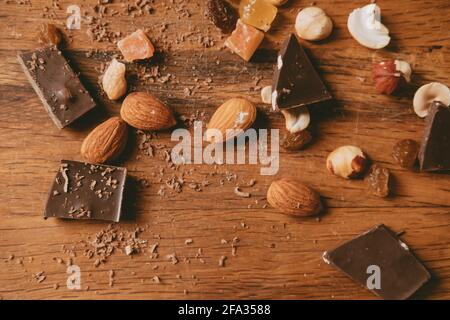 nuts and pieces of chocolate on wooden background. delicious chocolate bars with almond and hazelnuts on a brown background. Sweet food Stock Photo