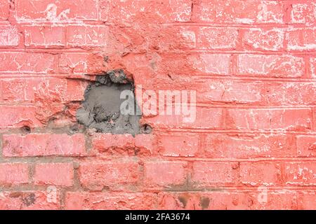 Old pink and red painted brick wall facade texture with carelessly cemented hole in the building, background repair. Stock Photo