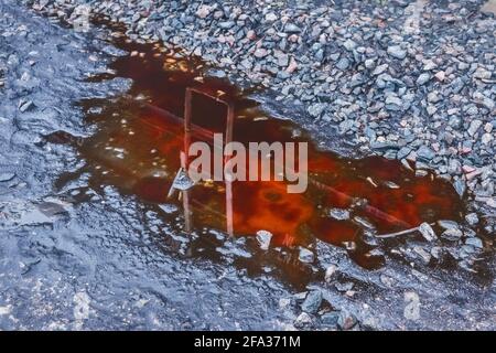 Puddle of red potash chemical fertilizer after rain on a crushed stones of agriculture industrial plant. Stock Photo