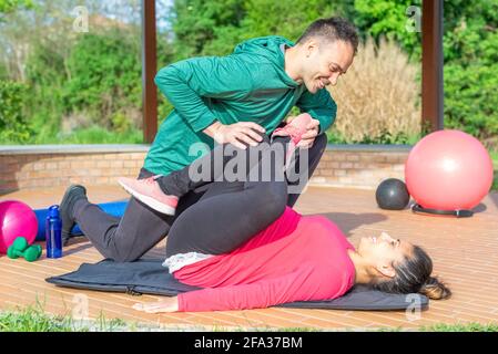 couple of a smiling personal trainer and a beautiful woman doing workout exercise outdoor.friends practicing stretching after gym session outside. fit Stock Photo