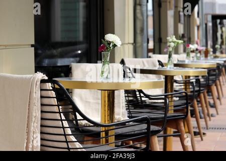 Street cafe with empty tables outdoor, city during coronavirus pandemic. Vases of flowers on a tables and vintage wooden chairs with warm plaids Stock Photo