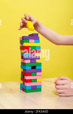 Hands close up playing a round of family game removing blocks from the tower made from colorful wooden blocks. Planning, risk, and strategy in busines Stock Photo