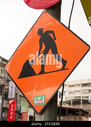 A diamond shaped standard road digging construction sign with a graphic of a worker wearing a traditional Asian, Oriental, Vietnamese style conical ha Stock Photo