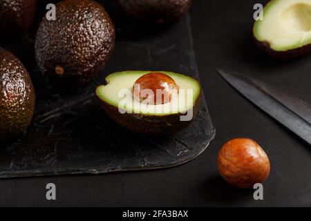 Sliced and whole organic avocado Hass with a knife on a black background. A source of essential fats, vitamins, trace elements, beta-carotene and omeg Stock Photo