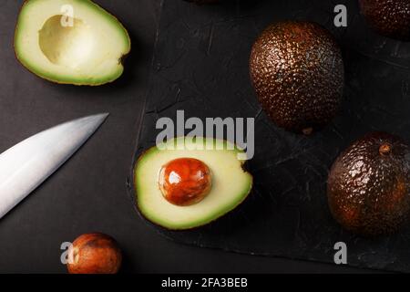 Sliced and whole organic avocado Hass with a knife on a black background. A source of essential fats, vitamins, trace elements, beta-carotene and omeg Stock Photo