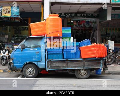 A small, blue pickup, utility truck fully loaded with orange, pink, yellow, green and blue plastic containers. In Taipei, Taiwan. Stock Photo