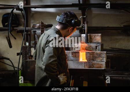 Back view of a man in protective glasses watching the traditional process of heating metal Stock Photo