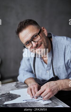 Craftsman artist making manual carving process using special instrument. Handmade work. Bearded middle aged man in apron and eyeglasses making linocut using cutting instrument. High quality image Stock Photo