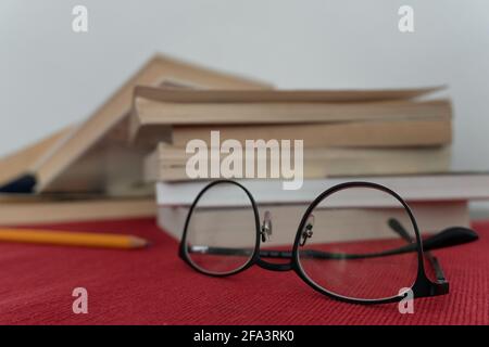 Eyeglasses in foreground and a book stack and pencil on the left in the background, lying on a red tablecloth. High quality photo Stock Photo