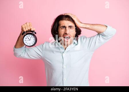 Photo of stressed funny guy hold clock oversleep wear spectacles blue shirt isolated on pink color background Stock Photo