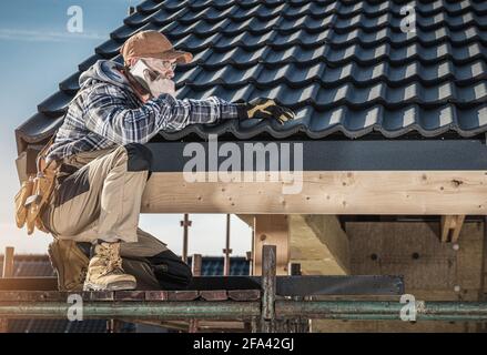 Caucasian Professional Roof Construction Worker in His 40s Making Phone Call While Staying on Scaffolding. Roofer Calling For Supply. Stock Photo