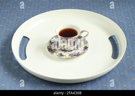 A white plastic tray with a cup of black tea stands on a blue tablecloth. Closeup Stock Photo