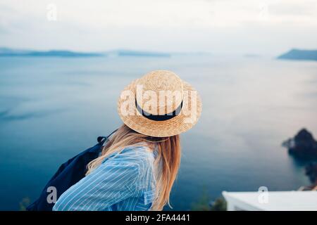 Tourist woman walking on Santorini island, Greece enjoying sea landscape. Traveler with backpack enjoys Caldera view in Oia Stock Photo