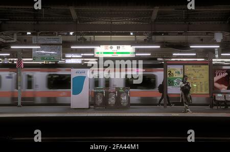 Tokyo, Japan - October 20 2020: Night view of a platform at Nakano Station, with a moving train and a few commuters visible Stock Photo