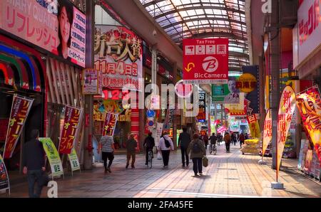 Osaka, Japan - November 5 2020: Pedestrians walk along a covered shopping street lined with shops and colorful signage in central Osaka on a sunny day Stock Photo