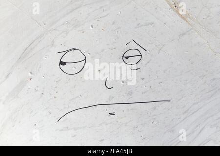 White marble veined surface on which a disgruntled face is drawn Stock Photo
