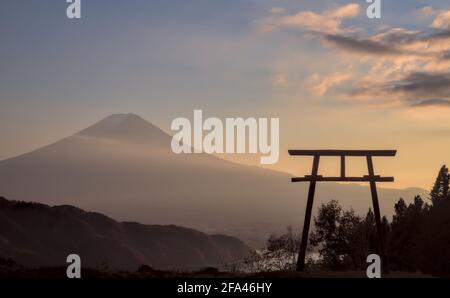 Late afternoon view of a torii gate and Mount Fuji under a partly-cloudy blue and yellow sunset sky Stock Photo