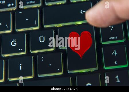 Finger clicking heart icon on black keyboard, online dating site Stock Photo