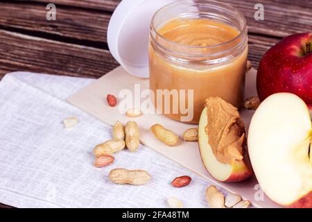 Fresh homemade crunchy peanut butter with nuts and apples on light wooden background in the kitchen. Stock Photo
