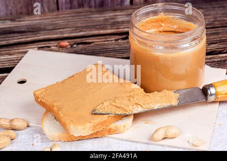 Homemade toasts  for breakfast with fresh crunchy peanut butter and nuts on light textile background. Stock Photo