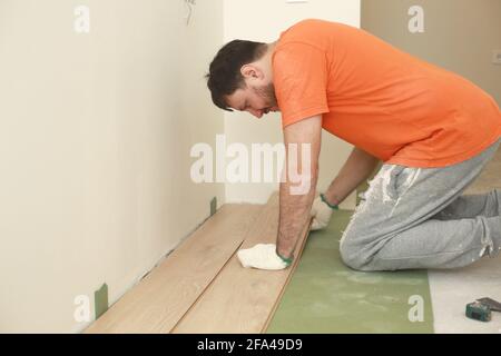 carpenter worker installing wooden laminate or parquet board during flooring work. Stock Photo