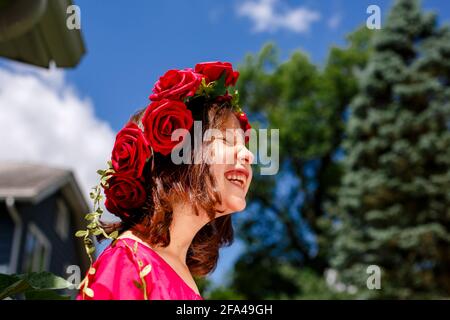 A laughing little girl with closed eyes wears a crown of roses Stock Photo