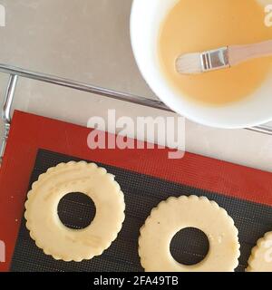 Cookie dough round flower shape on silicone mat, bowl with egg brush Stock Photo