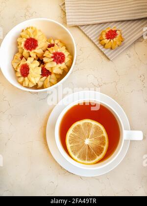 Cup of tea with lemon and bowl with jam cookies on a marble table Stock Photo