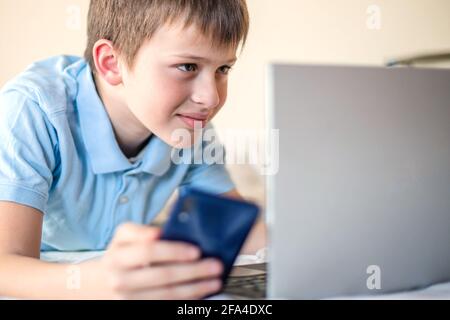 teenager learns remotely using online resources. Distance learning courses and lessons in web applications. child lies on sofa next to laptop and work Stock Photo