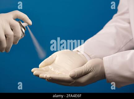 doctors clean hands with spray, hygiene in hospital, PPE standards, blue background Stock Photo