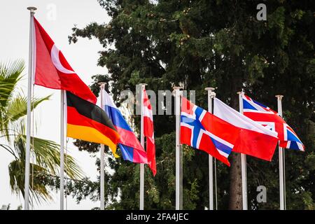 Row of national flags on flagpoles: Turkey, Germany, Russia, Denmark, Norway, Poland, Great Britain on the background of trees Stock Photo