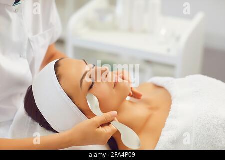 Satisfied woman lies with closed eyes in the masseur's office and receives a facial massage. Stock Photo