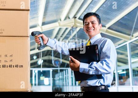 Young Indonesian man in a suit with a bar code scanner in a Asian warehouse Stock Photo
