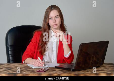 A woman sitting at a desk working with a laptop and notepad Stock Photo