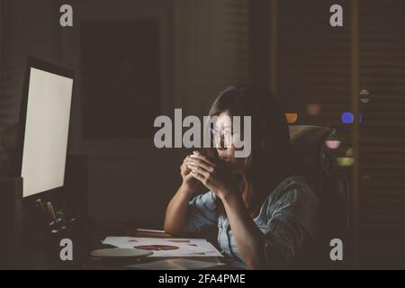 Portrait of Asian Businesswoman sitting and working hard on the table with front of computer desktop in workplace at late with serious action, Work ha Stock Photo