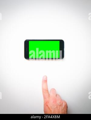 Male hand finger up to smartphone green screen on a white background curtains. Isolated blank space copypaste smartphone background mock up Stock Photo