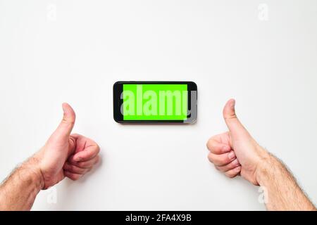 Male big hands and mobile smartphone with green screen in horizontal position background with two hand thumbs up finger. Mock up mobile screen blank s Stock Photo