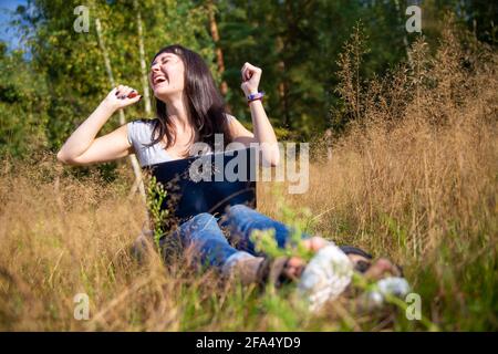 happy young woman with laptop on a sunny lawn. freelancer works in nature. student studies remotely on nature landscape outdoor Stock Photo