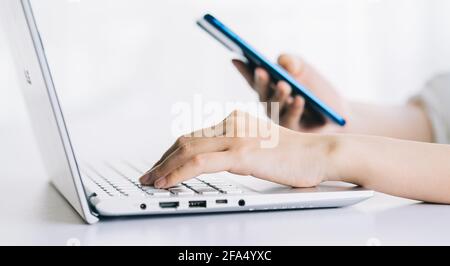 Asian woman using laptop and smartphone while working at modern home ...
